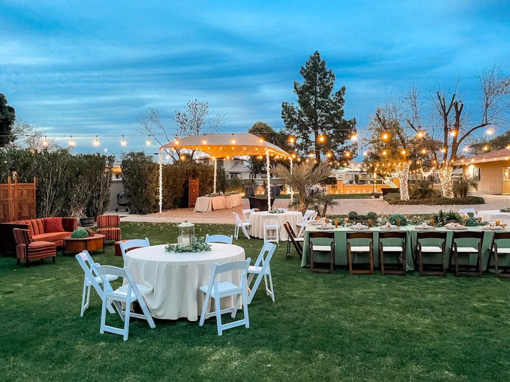 Private dinner set up in a Chandler, Arizona backyard at dusk with string lights, a long table and round tables
